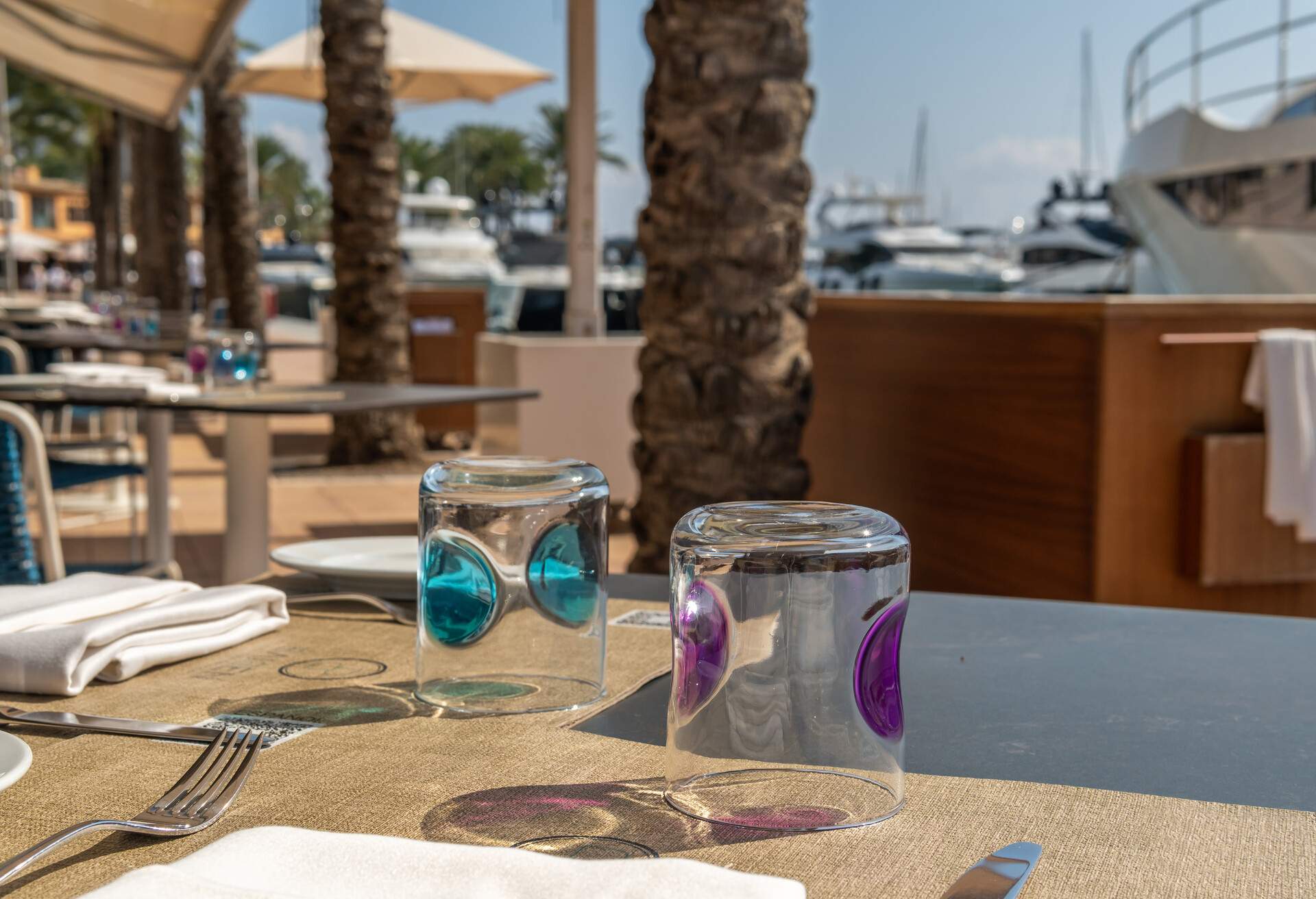 Close-up of a table on the terrace of a restaurant with QR code. In the background out of focus the touristic resort of Puerto Portals on the island of Mallorca. Marina with luxury yachts moored