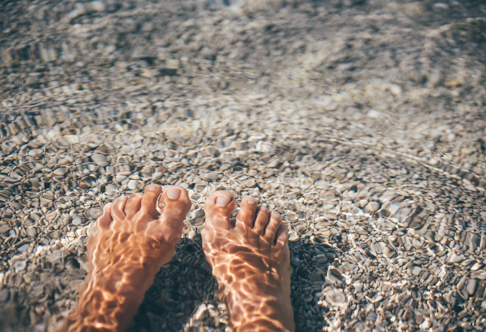 Personal perspective of woman's feet at clear turquoise water. 