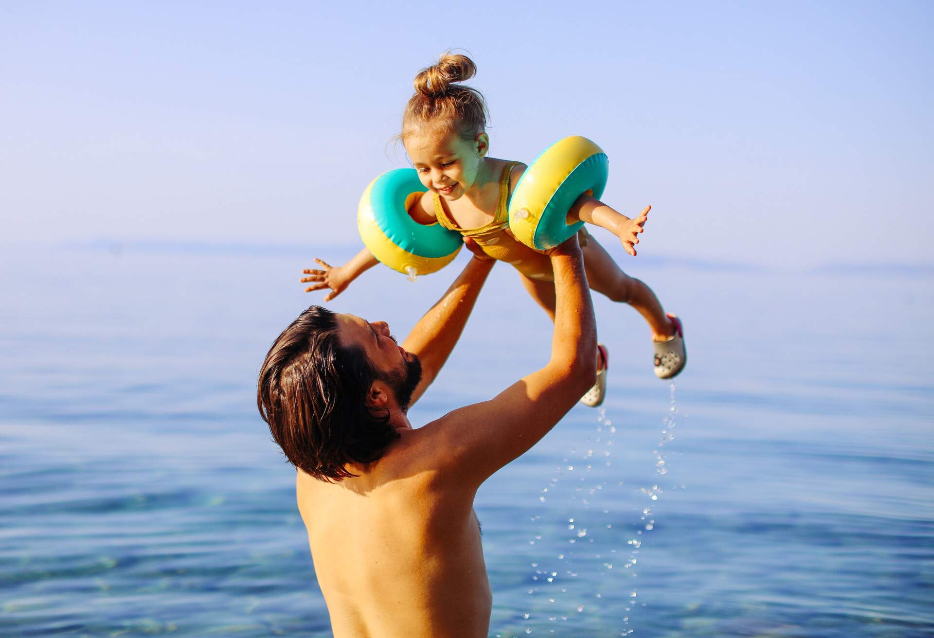 Father is throwing his daughter into the water with lots of splashing. Cute little girl having fun with parents in sea 
