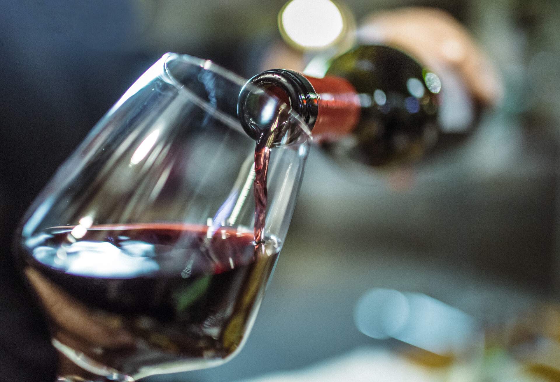 Unrecognizable person, holding a bottle of red wine, is pouring some red wine in a wine glass.