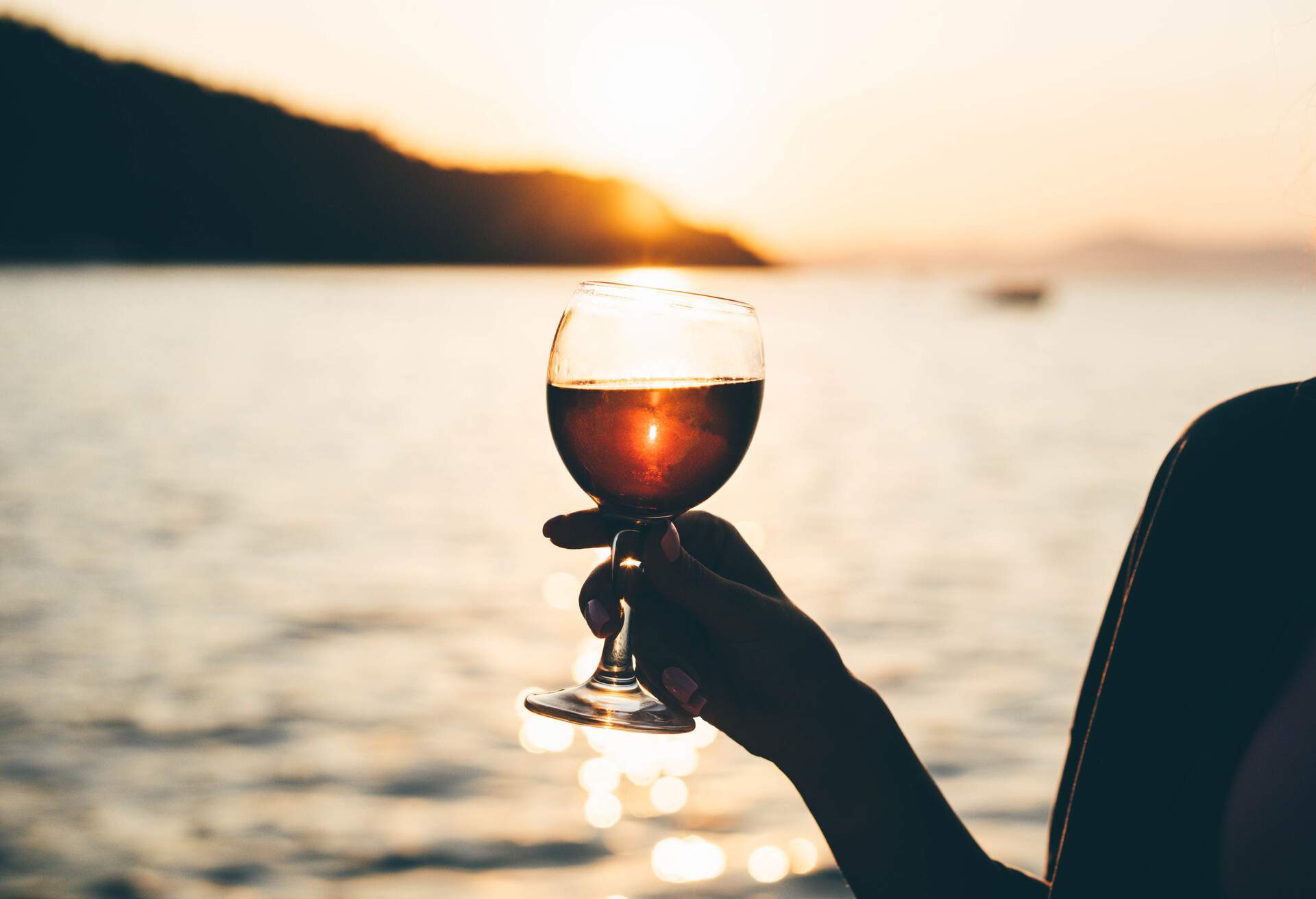 Woman drinking wine while enjoys sunset on the sailboat.