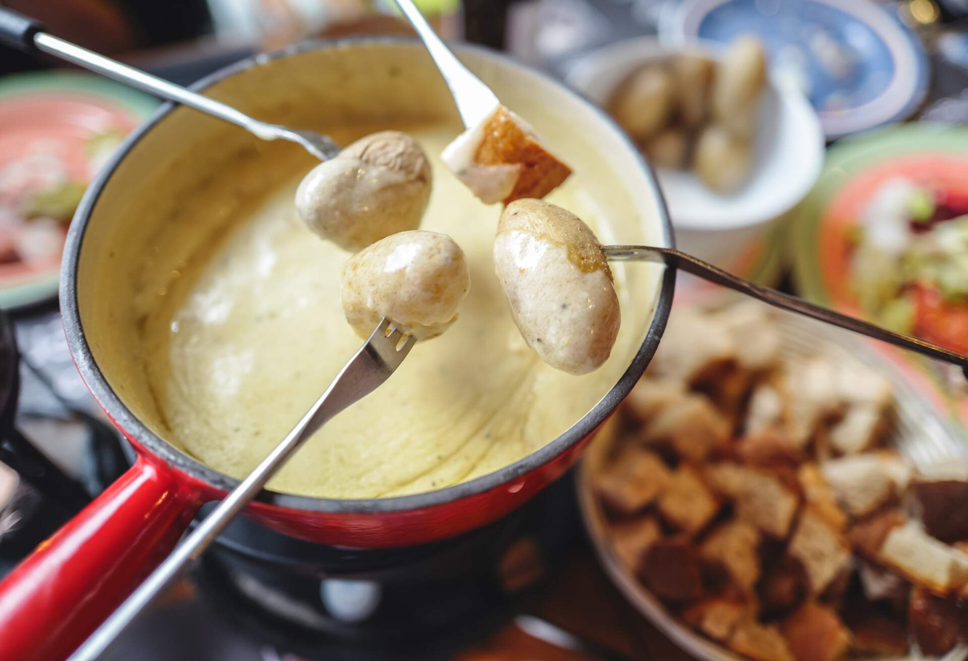 The famous authentic Swiss cheese fondue served in an earthenware pot, with cubed breads and potatoes dipping into rich melted cheese, landmark of Switzerland.