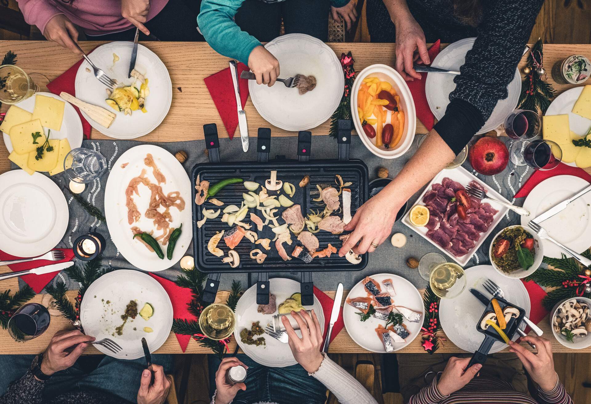 overhead view on family sitting around wooden table with raclette grill 