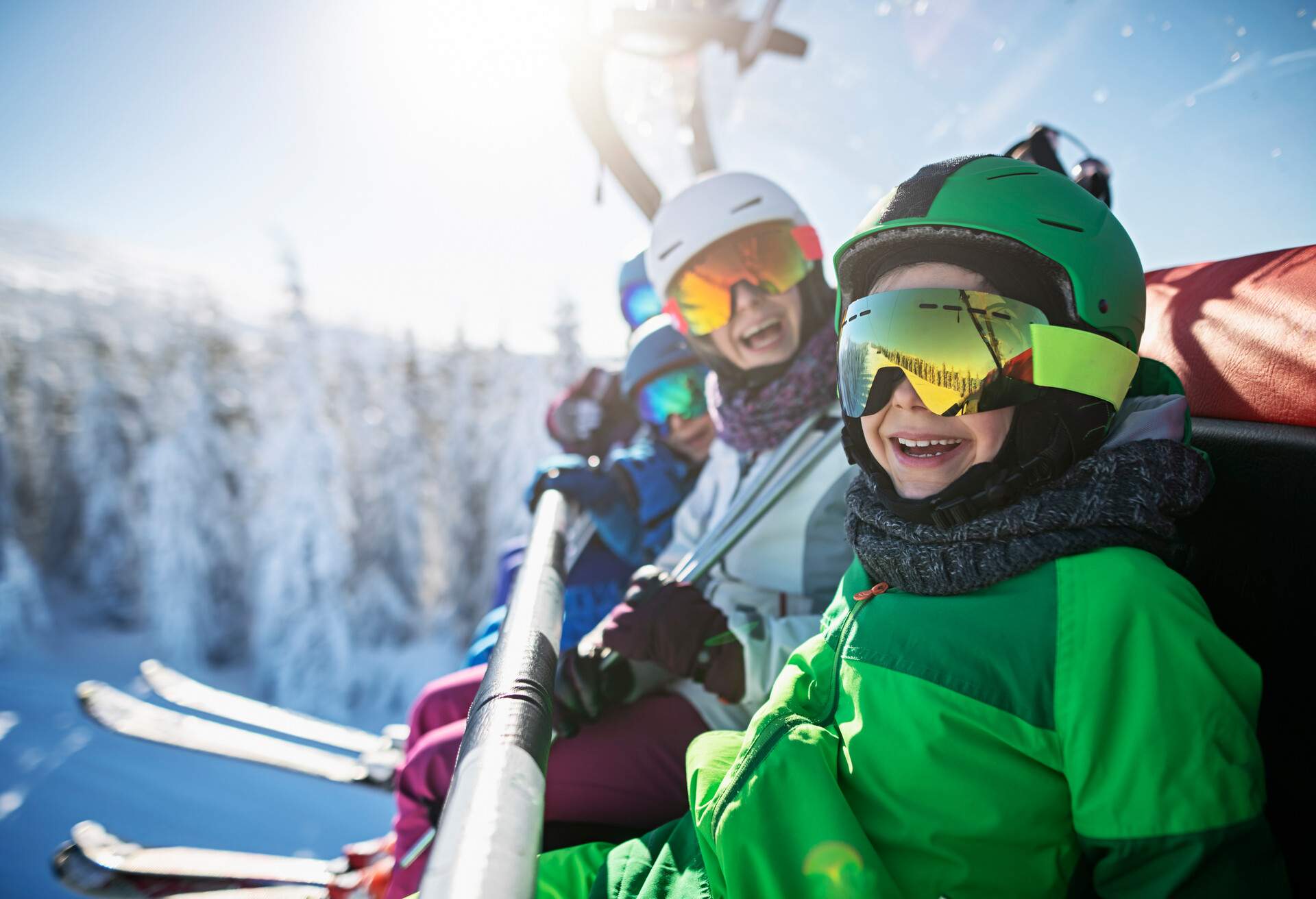 A smiling mother and kids in ski outfit sitting on a chairlift.