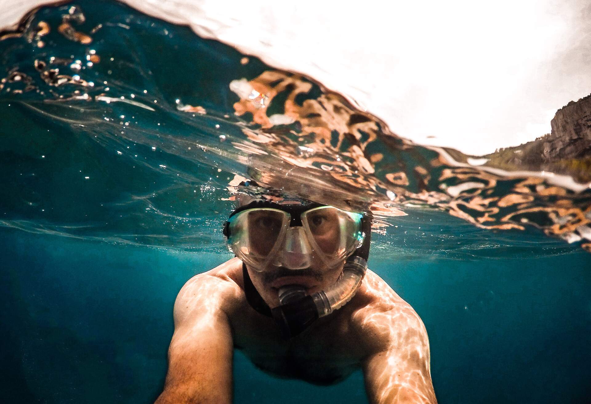 A man with SNORKELLING GOGGLES taking a picture underwater