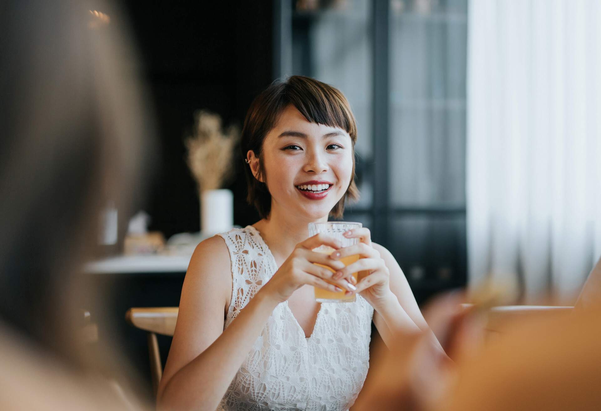 Portrait of smiling young Asian woman having fun and enjoying food and drinks in party with friends 
