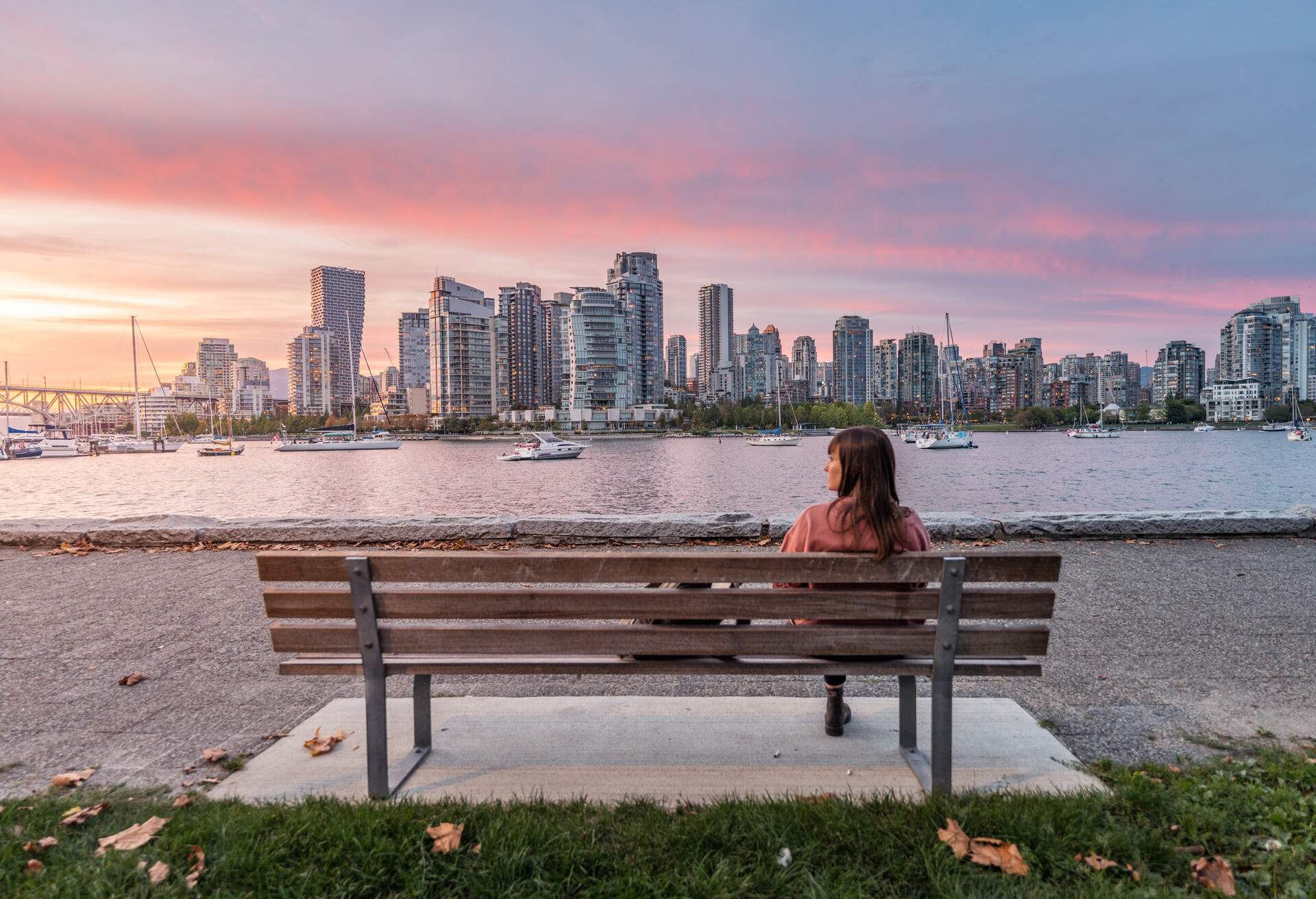 Panoramic Vancouver skyline at sunset from from the Island Park Walk. British Columbia, Canada. Woman sitting on a bench looking left