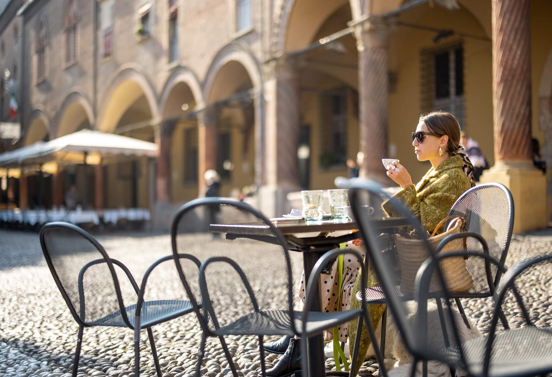 Stylish woman sitting at outdoor cafe in the old town of Bologna city. Italian measured lifestyle and street fashion concept. Idea of traveling Italy