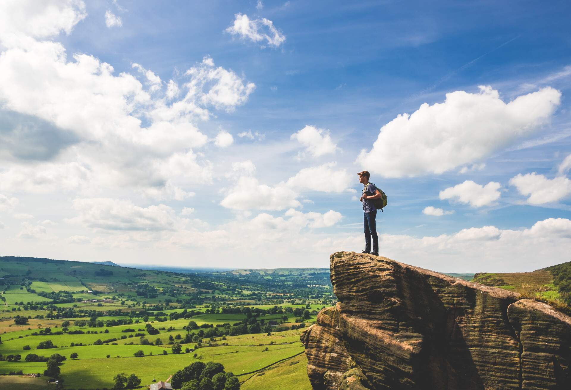 A teenage boy stands at the edge of a rocky outcropping while rambling along The Roaches in Peak District National Park, United Kingdom.
