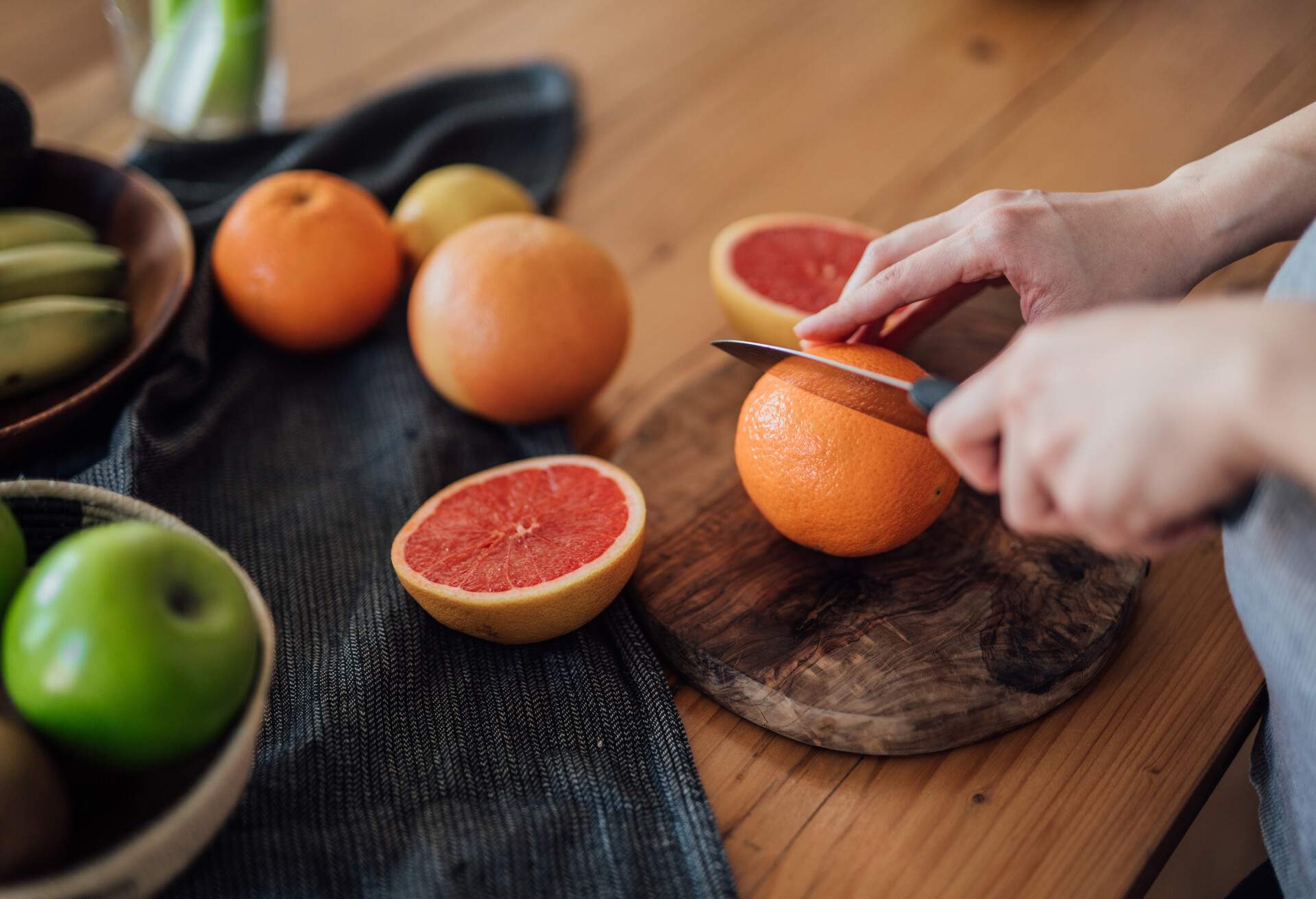 Close up shot of woman's hands chopping oranges and grapefruits for squeezing homemade juice in kitchen.