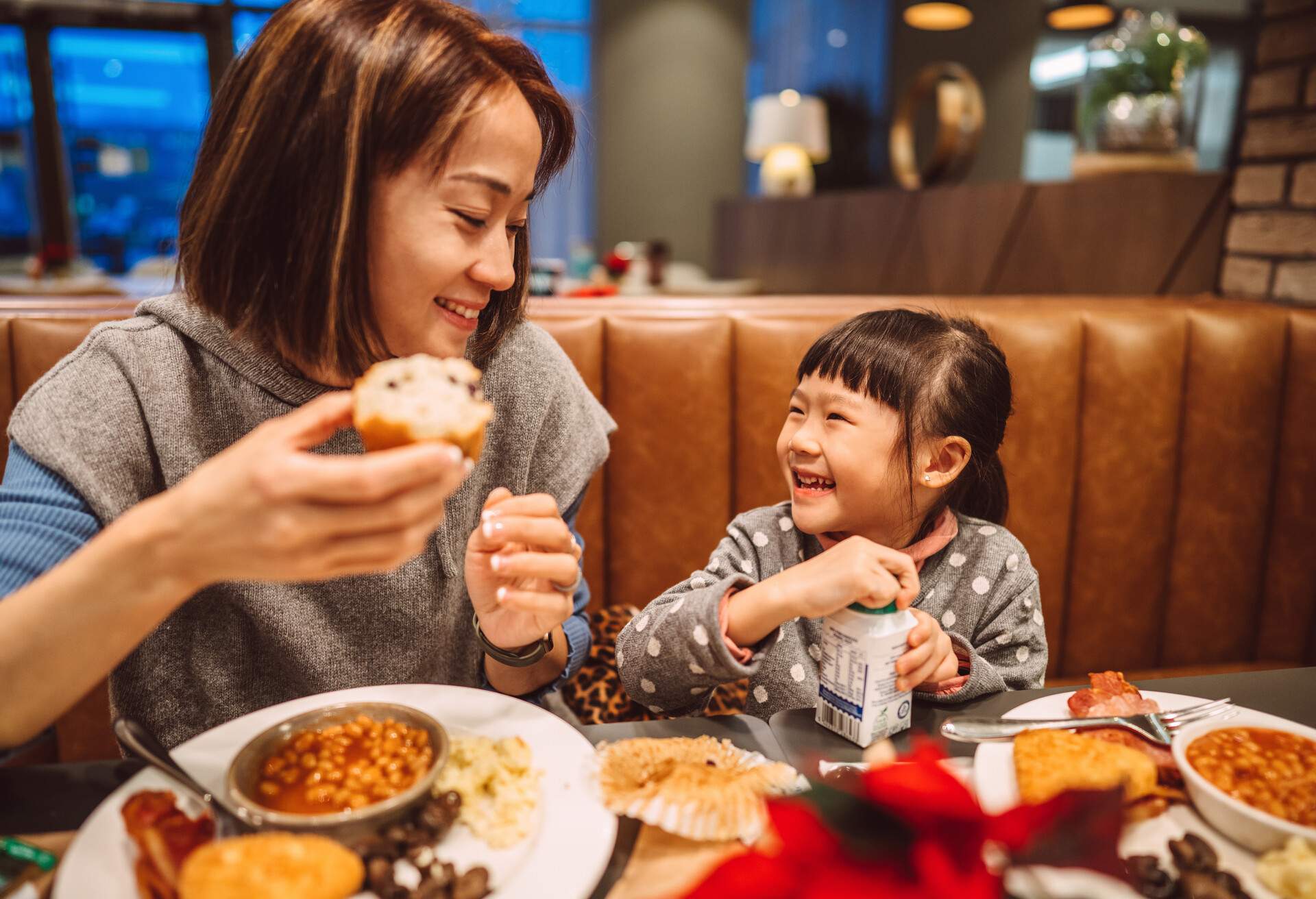Young Asian mom enjoying traditional English breakfast with her lovely daughter in a restaurant.