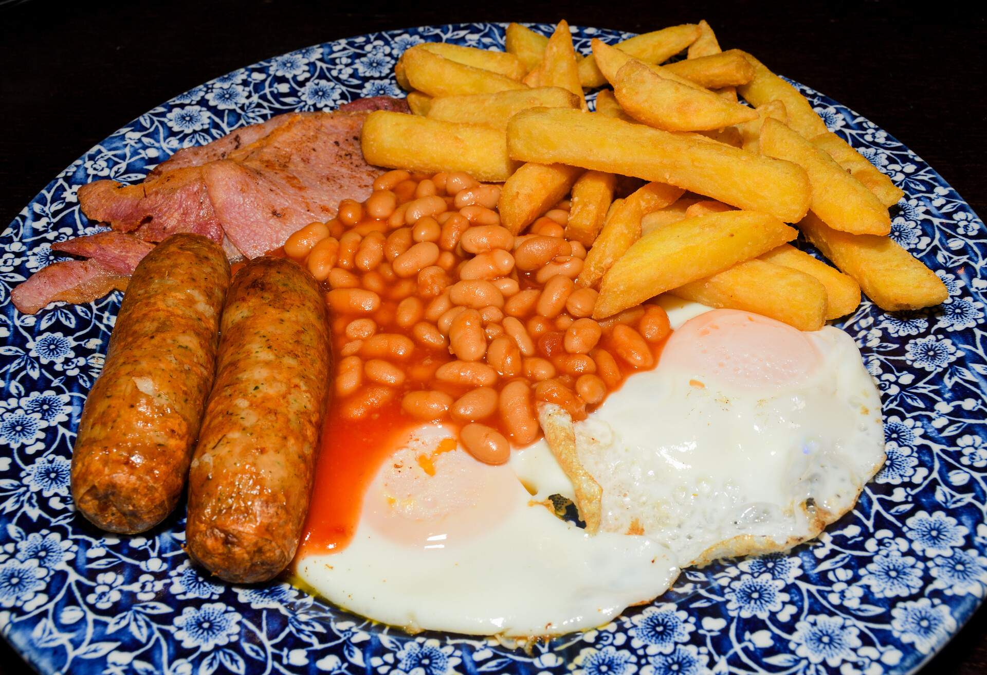 Traditional full English breakfast with fried eggs, sausages, beans, mushrooms, grilled tomatoes and bacon on wooden background. Top view