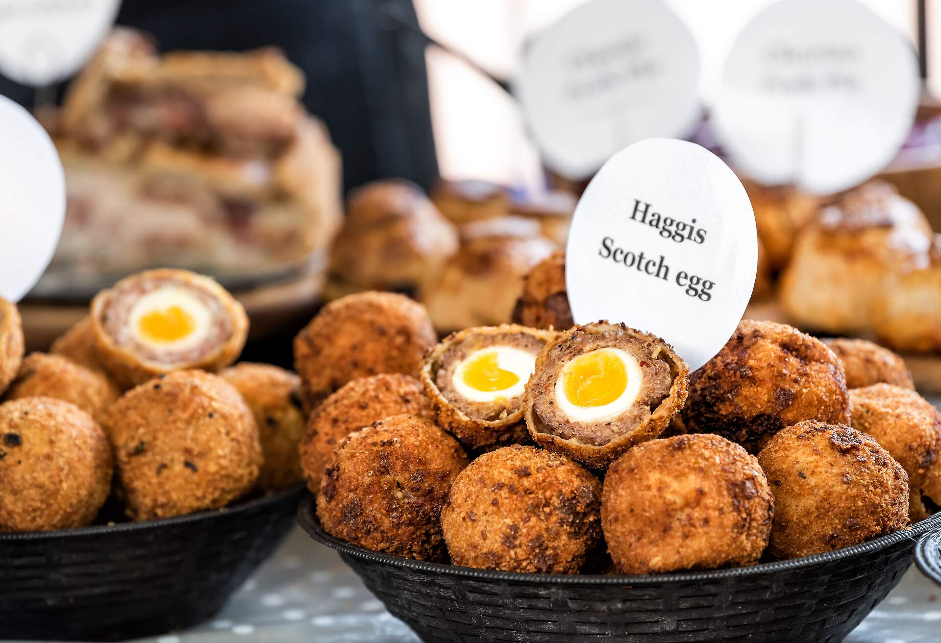 Closeup bowl of Haggis Scotch deep fried eggs with sign in market street food fair, cross section cut open, yellow yolk, breading tradition English food in London, United Kingdom
