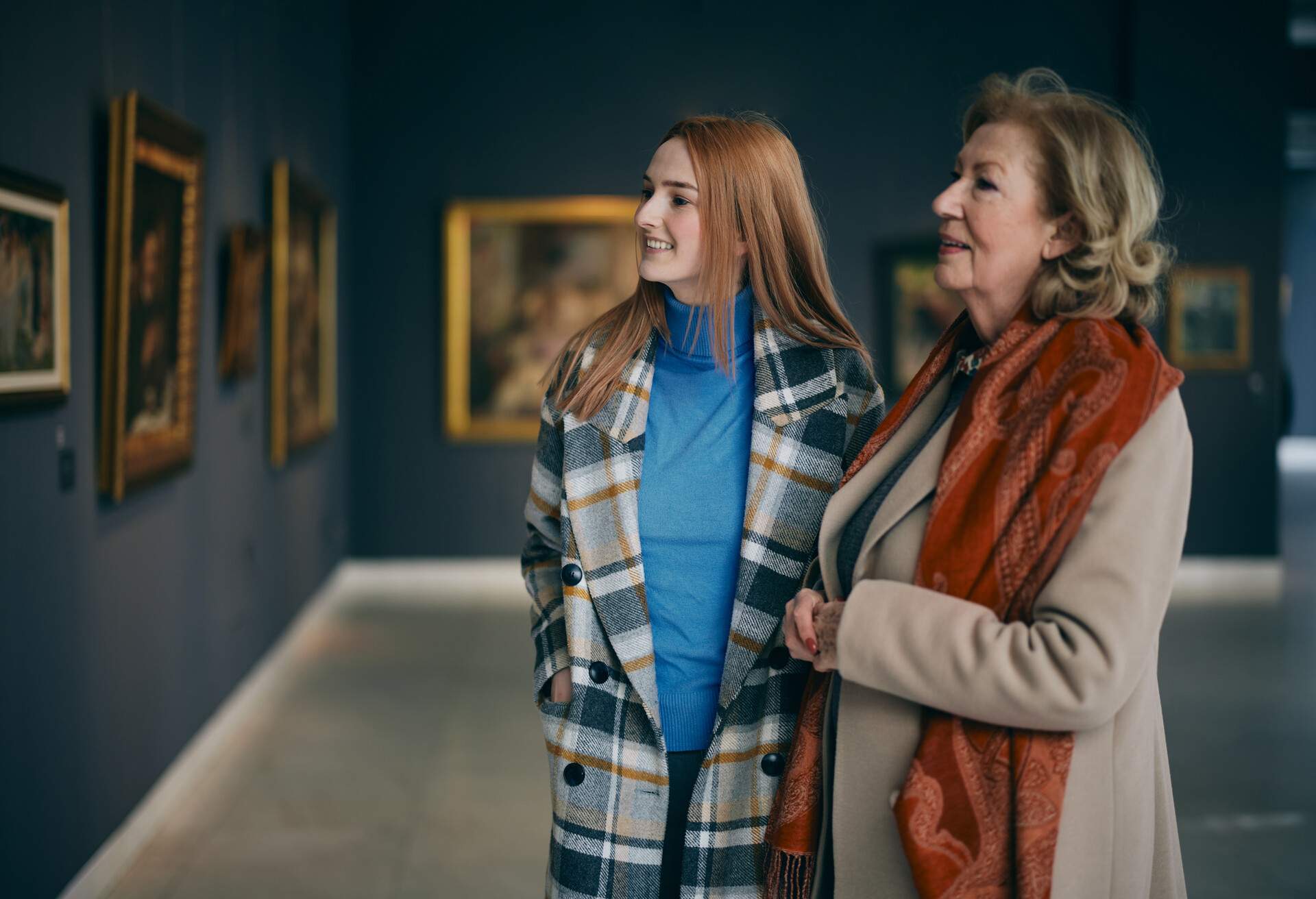Grandmother and adolescent granddaughter are looking at the paintings in the art gallery. 