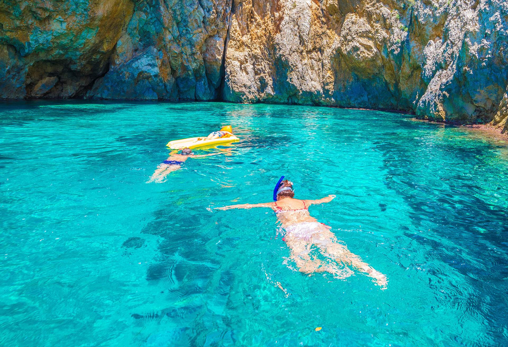 Three people snorkelling in a clear lagoon, with one riding a yellow inflatable boat.