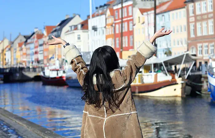 Woman on holiday standing with arms spread open in Nyhavn, Copenhagen, Denmark. - February 15, 2017