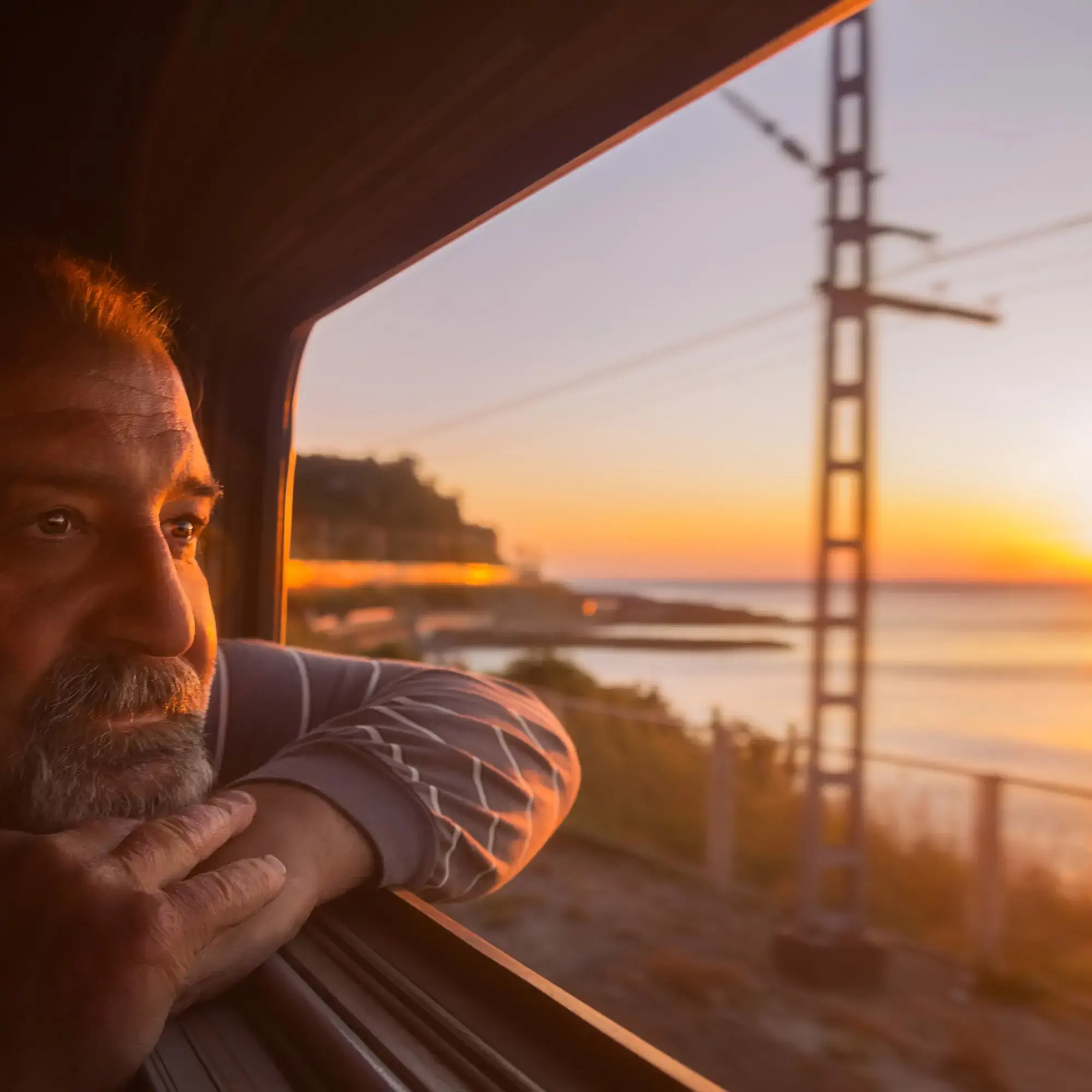 Elderly man admires sunset over the sea from open window of train