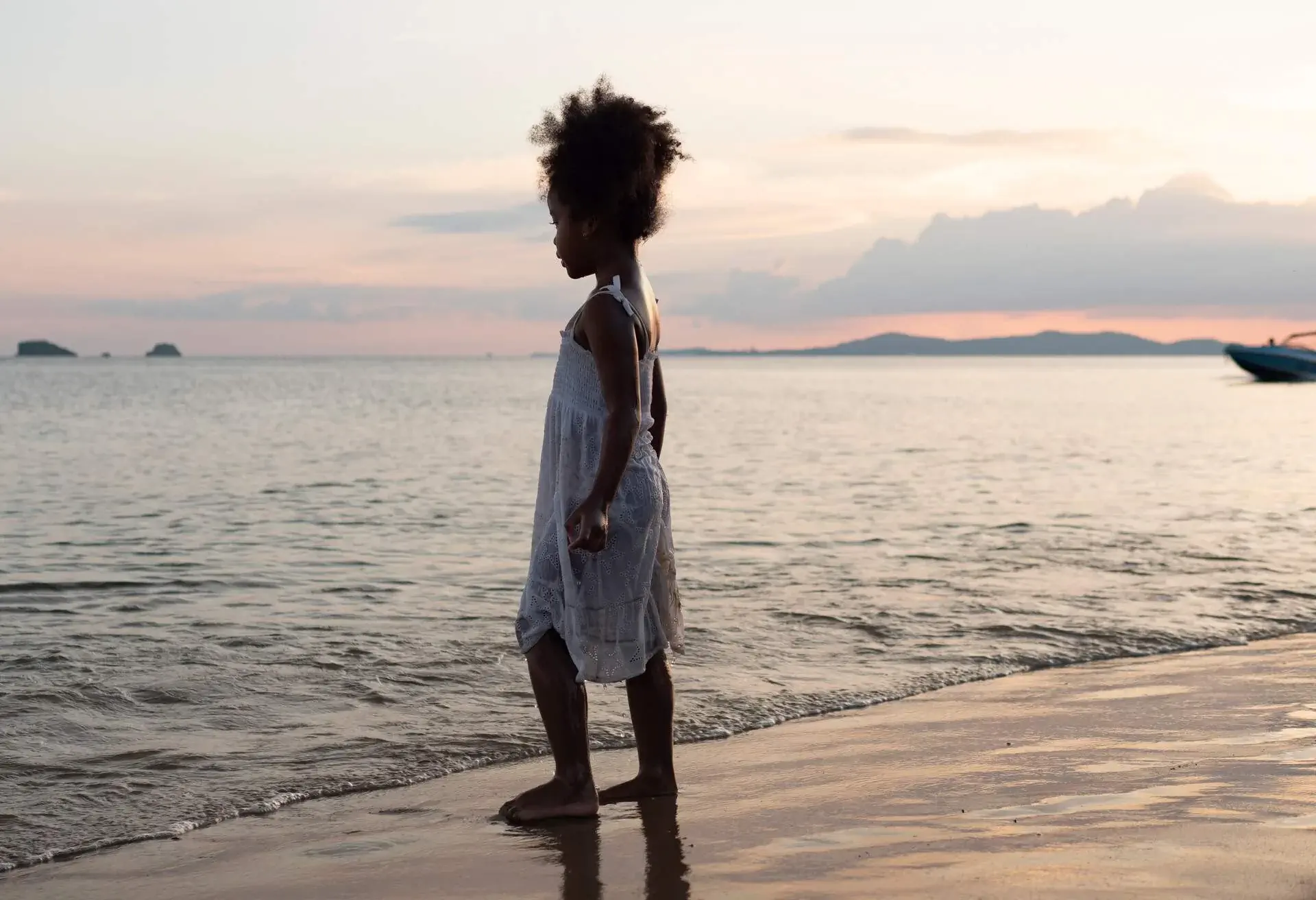 Rear view shot of a small girl standing on the beach and looking at the waves