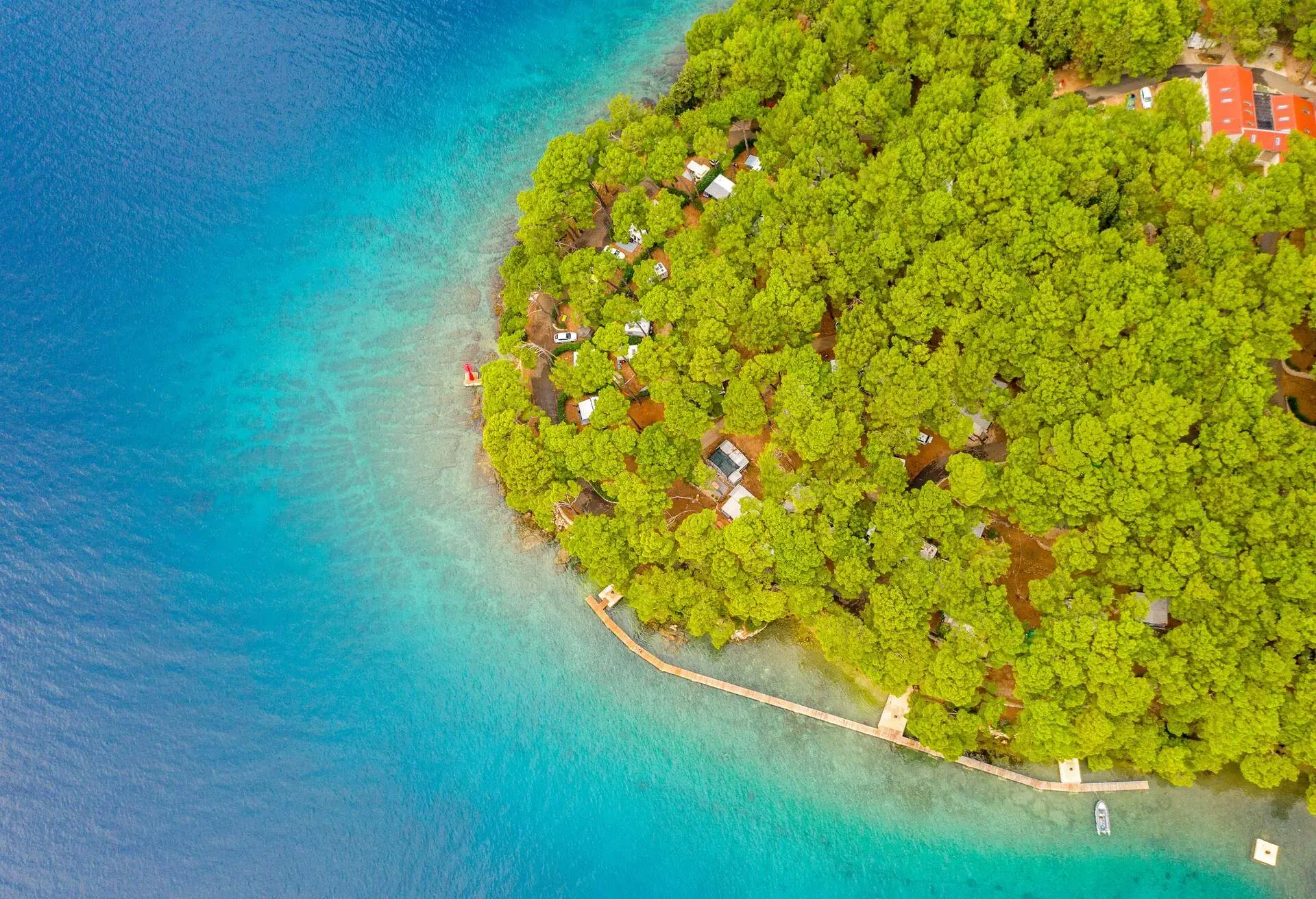 High angle aerial view shot of a landscape with buildings hidden in a green coastal forest, Cres Island, Croatia