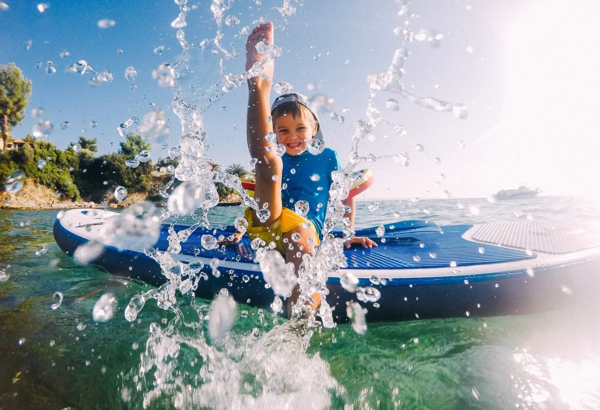 Photo of a little boy being playful and splashing in the sea, while sitting on a stand-up paddle board