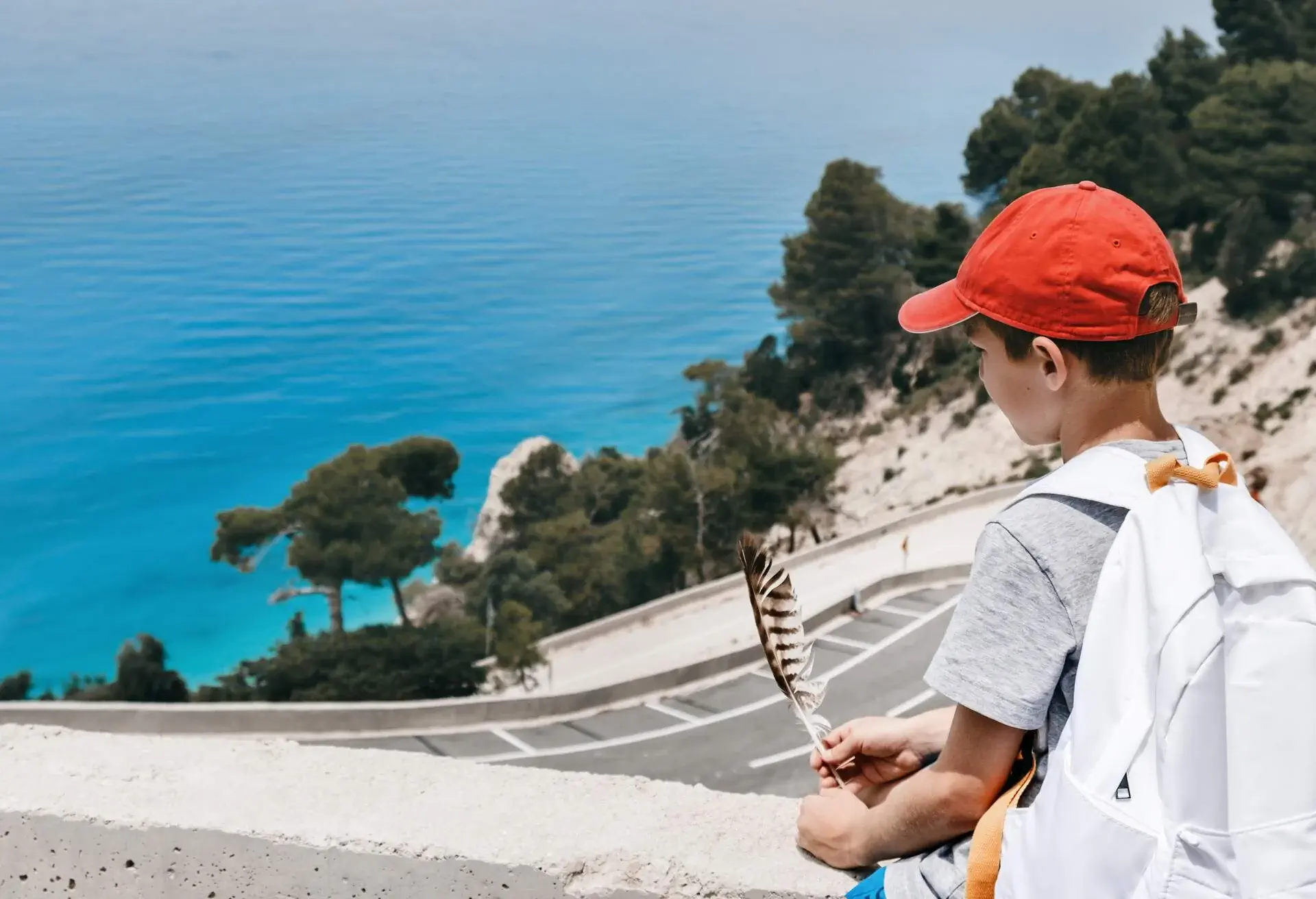 Young kid during summertime holidays looking at beautiful seascape and holding seagull feather, copy space.
