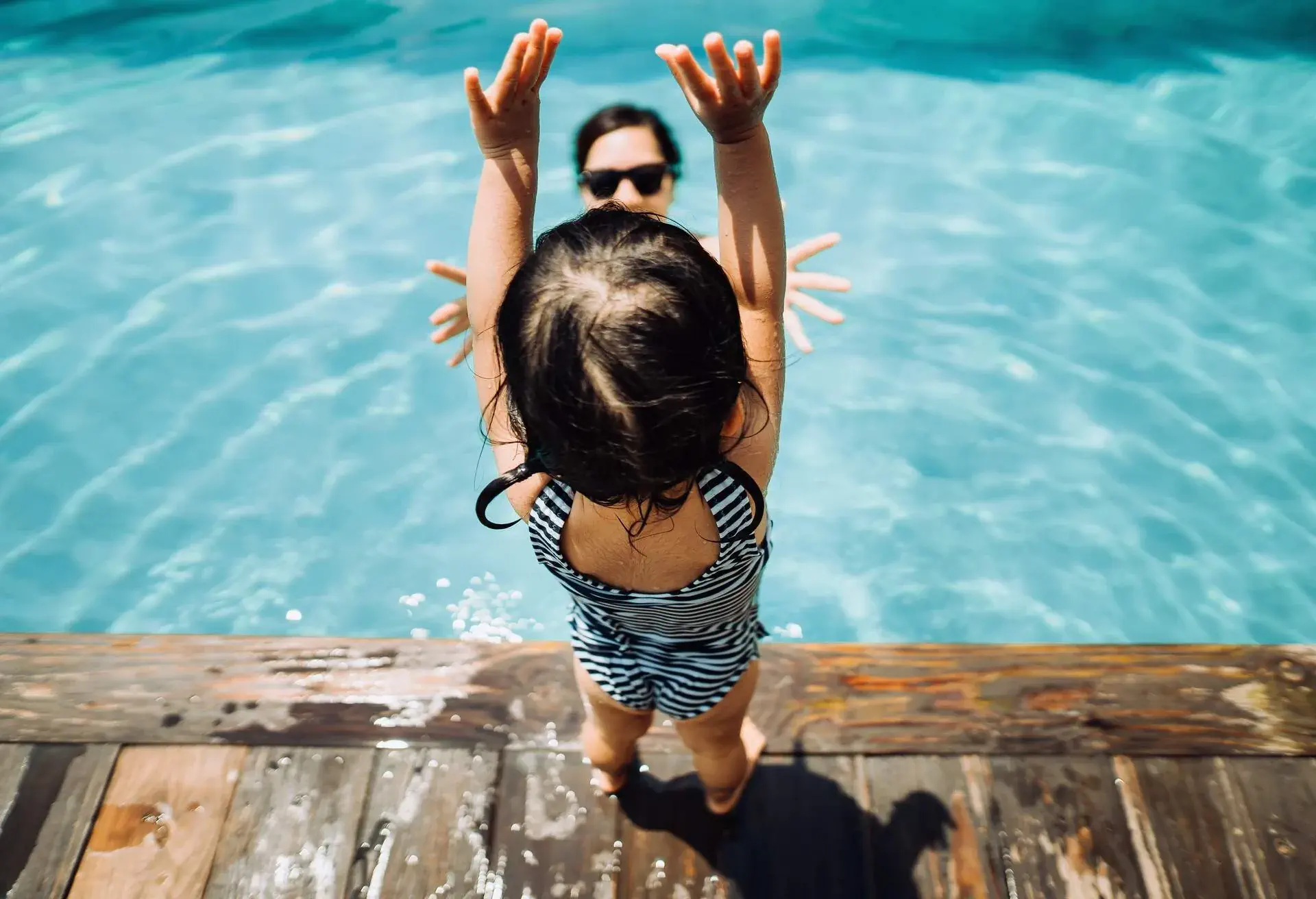 Overhead view of little Asian toddler girl having fun and jumping into her mother's arms in the swimming pool in Summer
