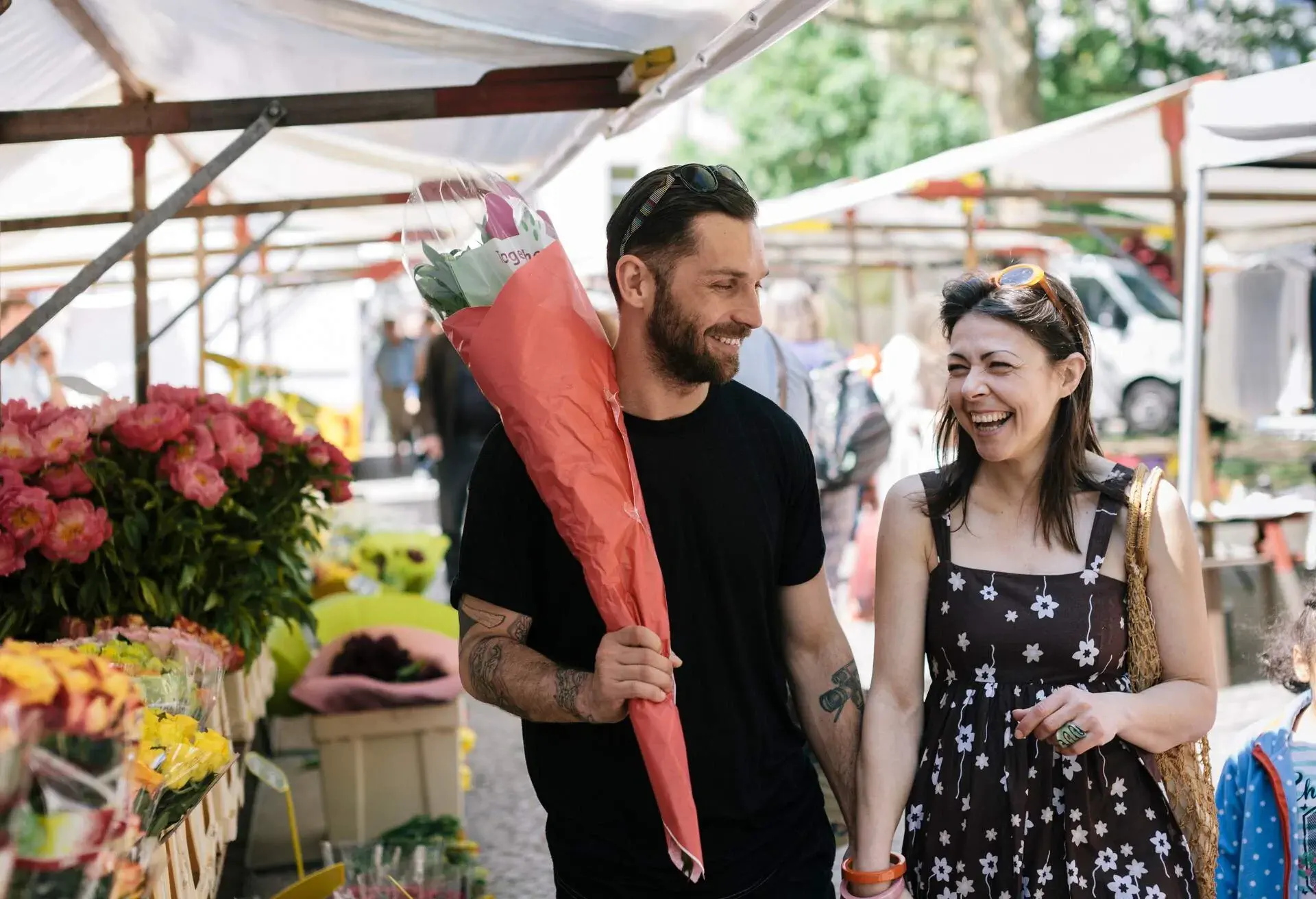Happy couple walking through Farmer's Market. Man is carrying a bunch of Flowers.