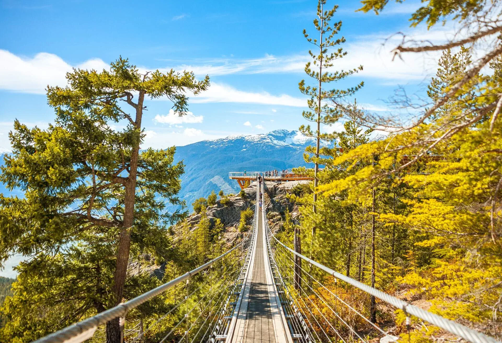 Squamish, BC, Canada - May 6th, 2019: View of the Sky Pilot Suspension Bridge with the Northwest Pacific Coast snowcapped mountains range on the background, against a sunny clear blue sky.