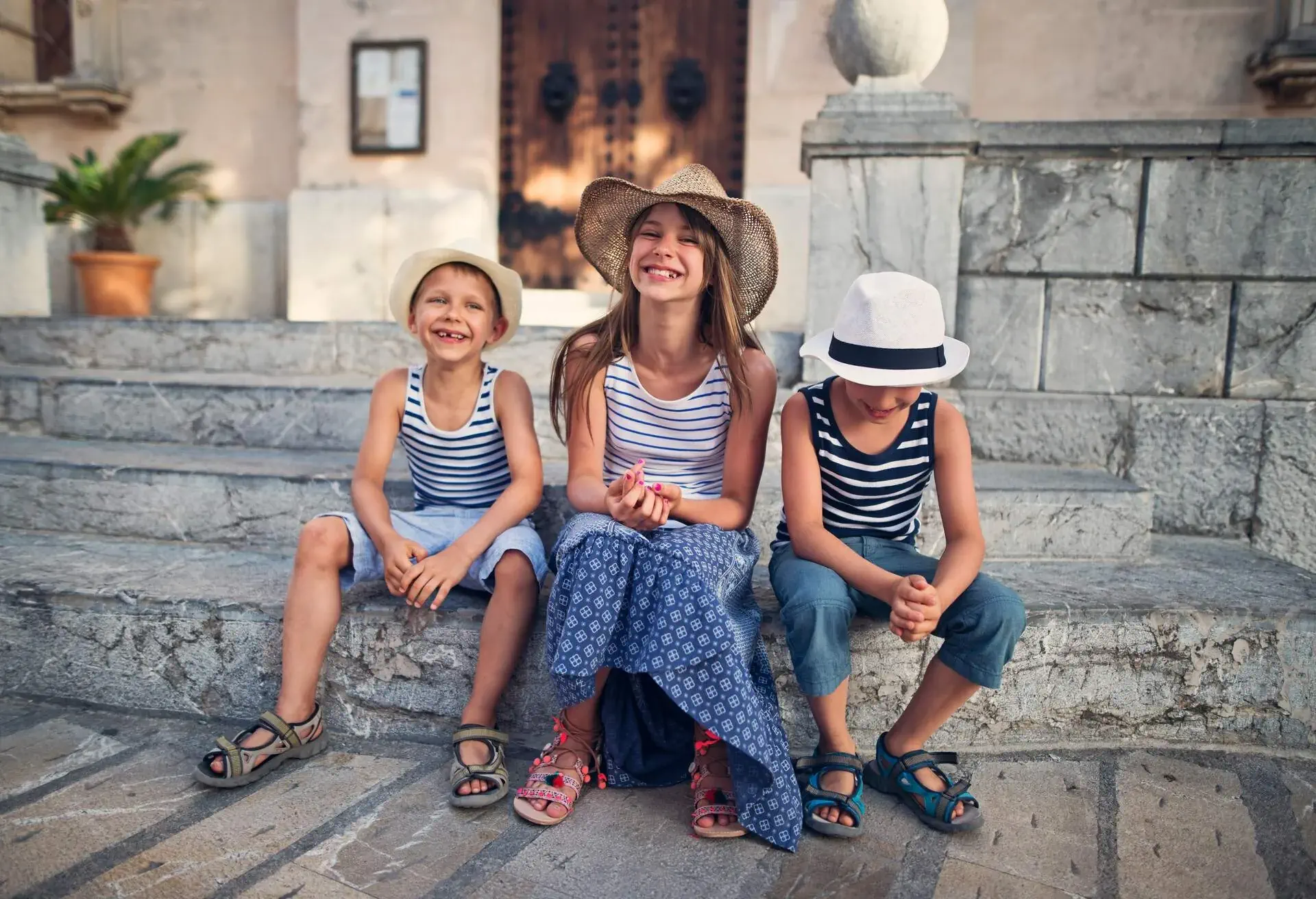 Sister and two brothers having fun visiting the beautiful Majorcan town of Alcudia. Kids are resting on stairs, having fun and laughing..