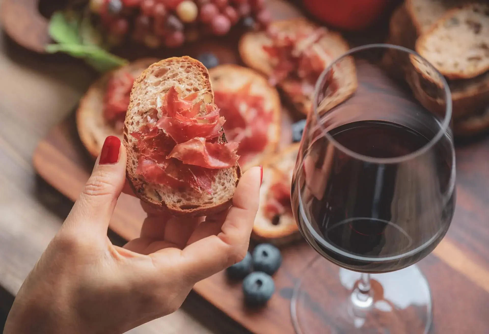 Selective foucs on finger holding ham jamon serrano and glasses of red wine on wooden board