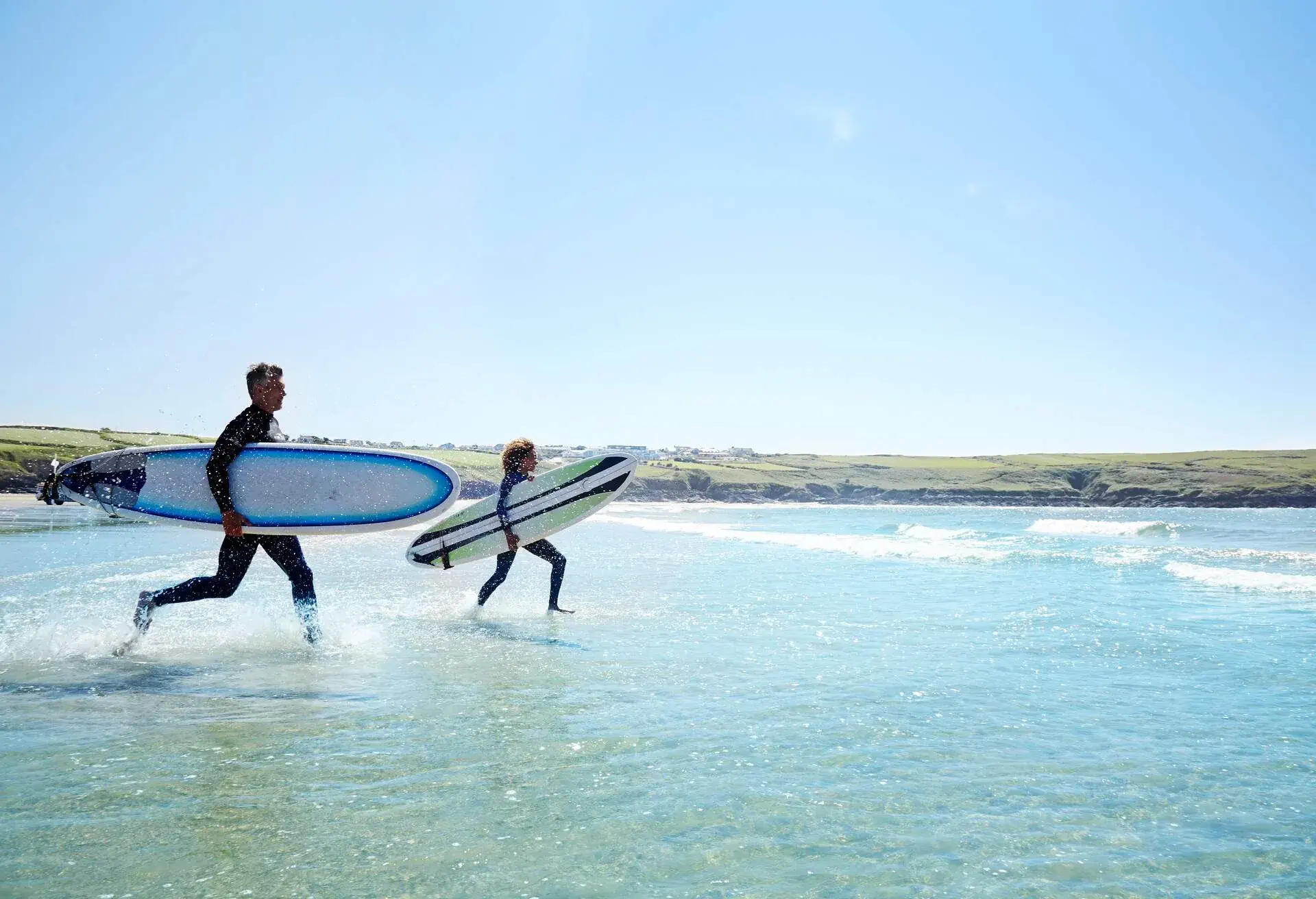 Surfers running into the waves with surfboards.